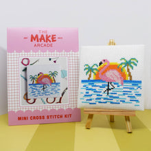 Load image into Gallery viewer, Make Arcade mini cross stitch kit envelope beside a finished flamingo beach cross stitch on a mini easel