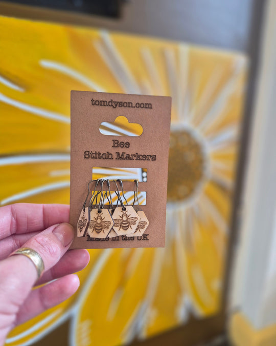 Hand holding Honey Comb Bees wooden stitch markers by Tom Dyson on a kraft card