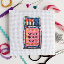Load image into Gallery viewer, Close-up of the finished matchbox cross stitch design reading Don't Burn Out on white Aida fabric with scissors and threads