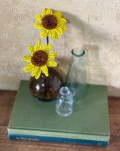 Load image into Gallery viewer, Two handmade yellow beaded sunflowers in a brown vase on a stack of books beside glass bottles