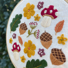 Load image into Gallery viewer, Close-up of Woodland Wonder embroidery stitching showing yellow flowers, acorns, leaves and red mushrooms