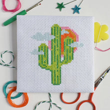 Load image into Gallery viewer, Close-up of the finished cactus cross stitch design on white Aida fabric with colourful threads and scissors
