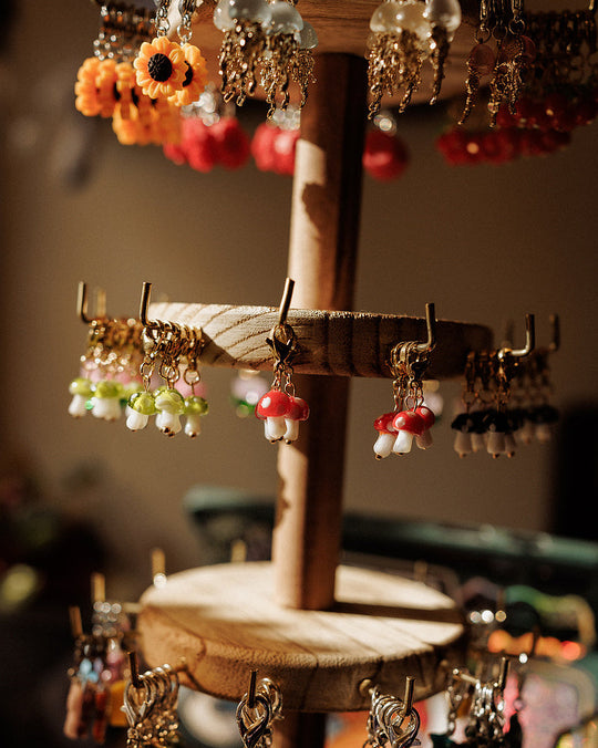 Handmade charm stitch markers by Till on a wooden display stand, including mushroom, flower and bead charms