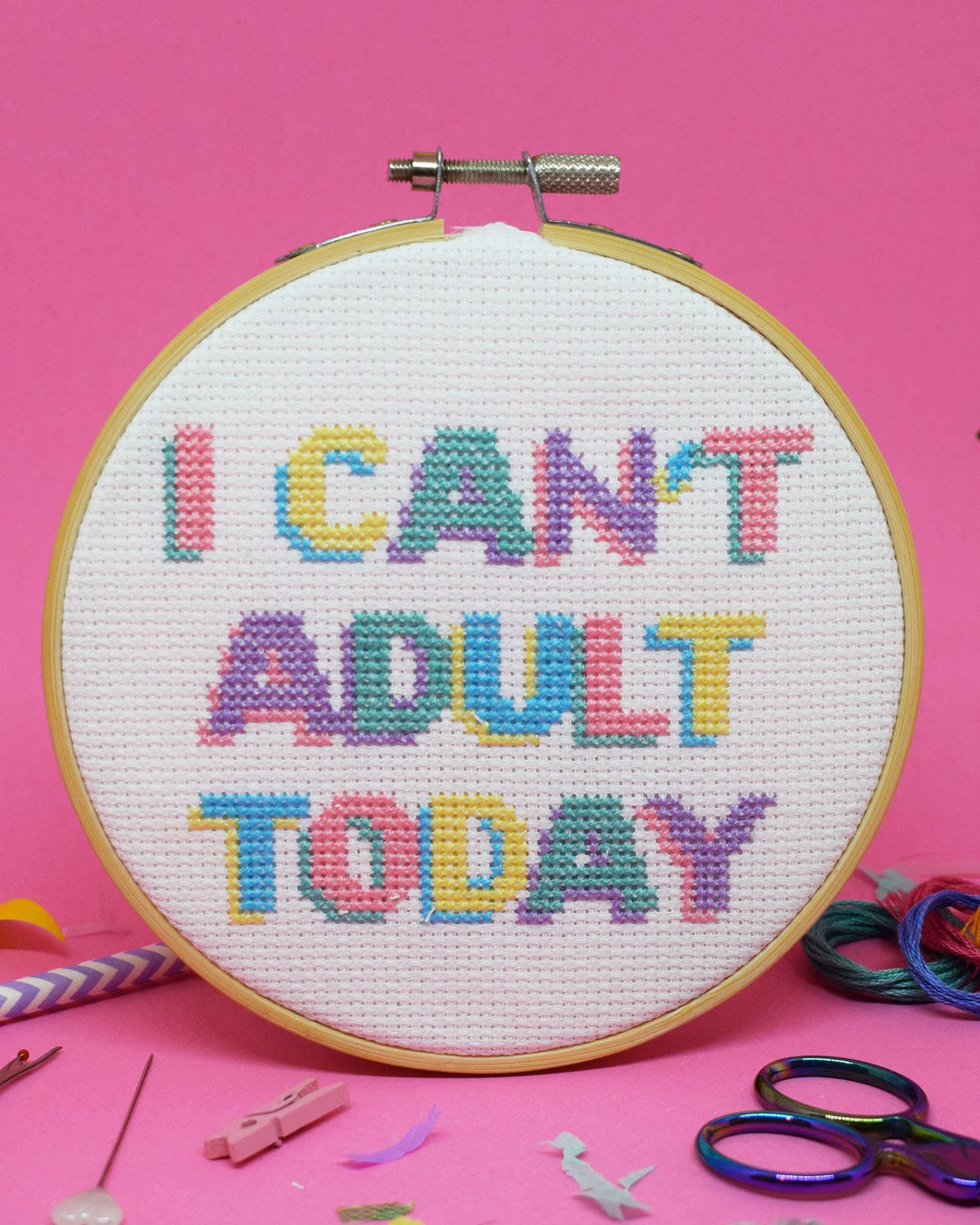 I Can't Adult Today cross stitch design in pastel colours stitched in a wooden hoop on a pink background