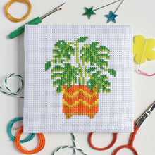 Load image into Gallery viewer, Close-up of the finished monstera plant cross stitch design on white Aida fabric with colourful threads and scissors
