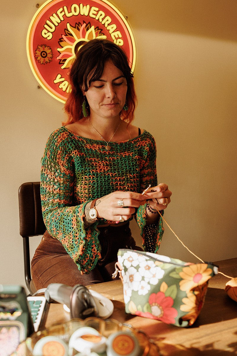 Sanchia crocheting under the Sunflower Raes neon sign