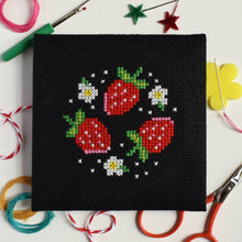 Load image into Gallery viewer, Close-up of the finished strawberry cross stitch design on black Aida fabric with colourful threads and scissors
