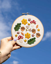 Load image into Gallery viewer, Woodland Wonder embroidery hoop with mushrooms, acorns and leaves held up against a blue sky
